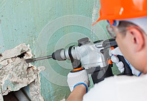 The builder is making hole in wall at construction site with hammer drill