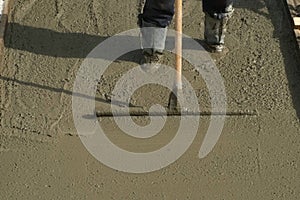 Builder mason worker leveling concrete with long trowel on construction site.