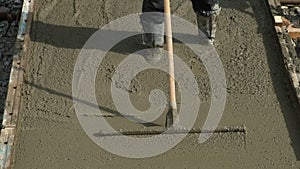 Builder mason worker leveling concrete with long trowel on construction site.