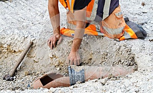 Builder in orange hi-viz clothing hand diggin and exposing damaged drainage pipe for repair