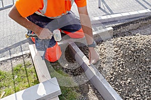Builder in orange ho-viz protective closing placing edging pin kerb into semi-dry concrete using a string line to keep them