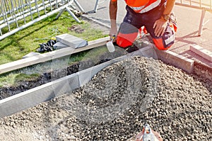 Builder in orange ho-viz protective closing placing edging pin kerb into semi-dry concrete using a string line to keep them