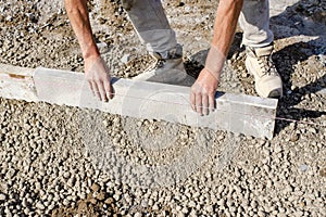 Builder placing edging pin kerb on semi-dry concrete using a string line to keep them straight during construction