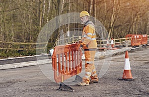 Builder placing safety barriers and red traffic cones during roadworks