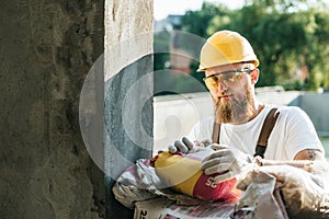builder in protective googles and hardhat opening bag of cement