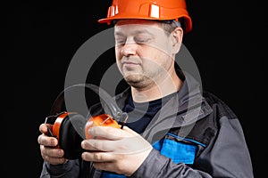 Builder in a protective helmet with noise-cancelling headphones in his hands on a black background