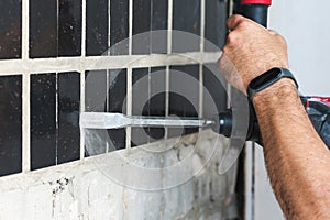 Builder with a puncher dismantles old tiles from a concrete wall