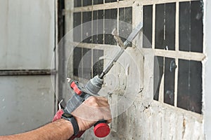 Builder with a puncher dismantles old tiles from a concrete wall