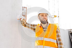 Builder repairman, foreman in safety helmet and vest works at his workplace in a building under construction