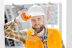 Builder repairman, foreman in safety helmet and vest works at his workplace in a building under construction