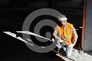 Builder repairman, foreman in safety helmet and vest works at his workplace in a building under construction