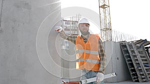 Builder repairman, foreman in safety helmet and vest works at his workplace in a building under construction