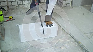 Builder sawing aerated concrete block along drawn line with hand saw