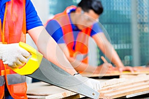 Builder sawing a wood board of building or construction site