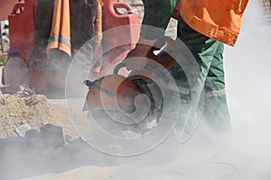 A builder saws a concrete block with a circular saw repairing the road.