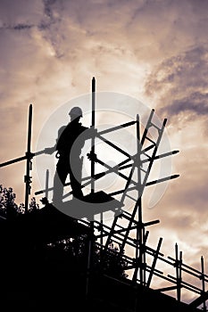 Builder on scaffolding building site at sunset