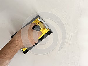 A builder smooths a wall after plastering using a sanding tool. The image depicts construction work and interior