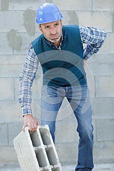 Builder suffering from back ache while moving cement block