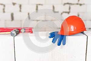 Builder tools lays aerated concrete block at a construction site. Objects. Hemlet, gloves, water lavel, hammer on brick wall