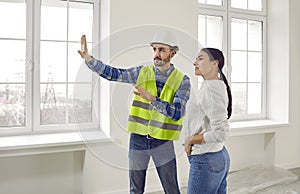 Builder in a uniform with a helmet talking to a woman about renovation in her new house or apartment