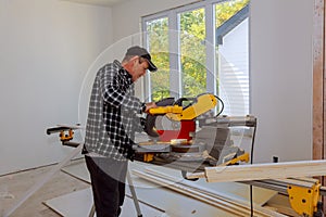 Builder uses circular saw tool to cut wood baseboard woodwork