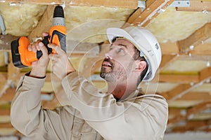 builder using cordless drill on wooden ceiling joist