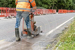 Builder using petrol powered road saw with dimond blade to cut asphalte road surface