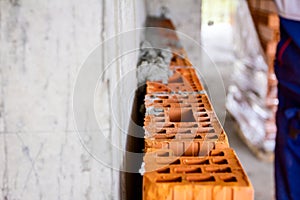 Builder using spatula to set up mortar over red brick