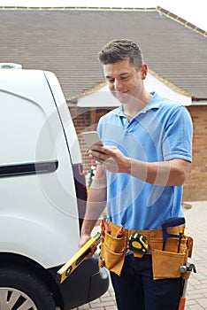 Builder With Van Checking Text Messages On Mobile Phone Outside