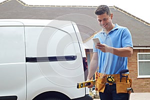 Builder With Van Checking Text Messages On Mobile Phone Outside