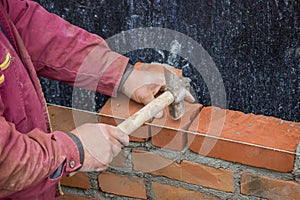 Builder worker with bricklayer hammer laying solid clay brick