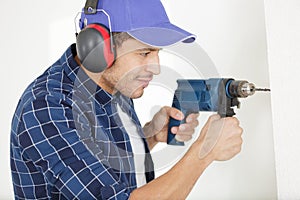builder worker with drill making hole in wall