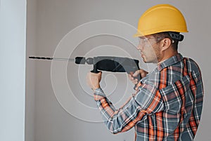 Builder worker with equipment making hole in wall at construction site