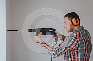 Builder worker with equipment making hole in wall at construction site