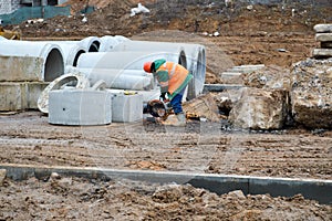 A builder worker in a helmet and a robe works with an industrial iron saw grinder at a construction site with an industrial saw