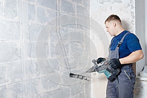 Builder worker man with hammer drill perforator equipment making hole in gray wall construction
