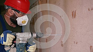 Builder working with rotary hammer drill. Contractor drills holes in concrete with jackhammer to demolish the wall for