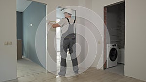 A builder in working uniform checks the size and quality of doorways in a new apartment