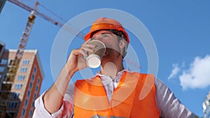 Builder in working uniform drinking coffee while standing construction site. Business, building, industry concept. Slow