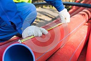 Builder`s hands in white gloves, measure the length of the red plastic pipe, yellow tape measure, to mark the size, close-up