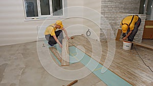 Builders laying wooden laminate boards on floor.