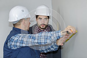 Builders measuring wall with tape measure