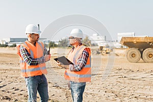 Builders in orange vests and helmets working on the road construction field