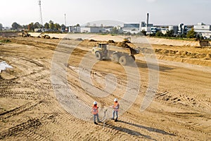 Builders in orange vests and helmets working on the road construction field