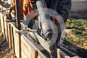 Builders pouring concrete with pump truck in wooden formwork with reinforcement. Workers pouring concrete in formwork for