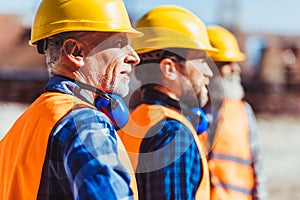 Builders in reflective vests and hardhats standing together at construction site, looking