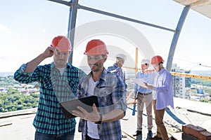 Builders On Site Working With Plan Of Construction Project On Tablet Computer Over Team Of Apprentices Holding Blueprint