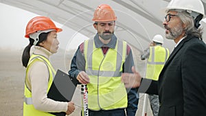 Builders talking at construction site while architect coming discussing project gesturing