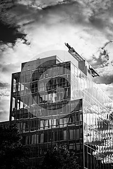 Building on a background of the cloudy sky.  The building appears crooked through the reflection of light.  Black and white