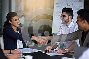 Building business relationships. Shot of two businesspeople shaking hands together in a boardroom while colleagues look